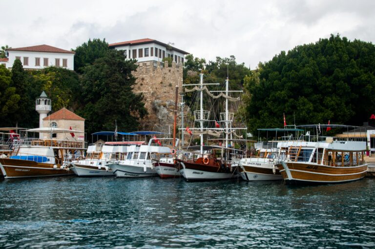 Small boats docked at a scenic harbor with lush greenery and historic architecture.